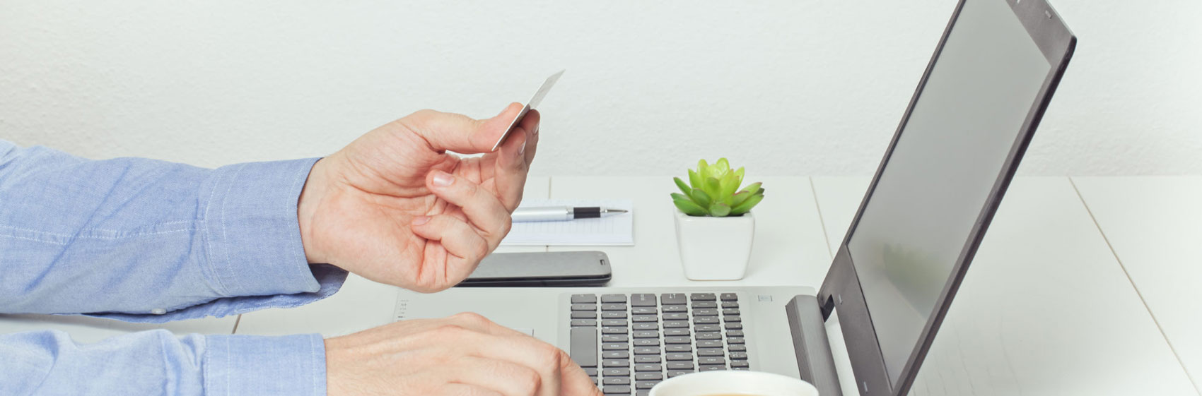 a person types their credit card number into something on their computer. One hand holds the credit card while the other hand types on the laptop.