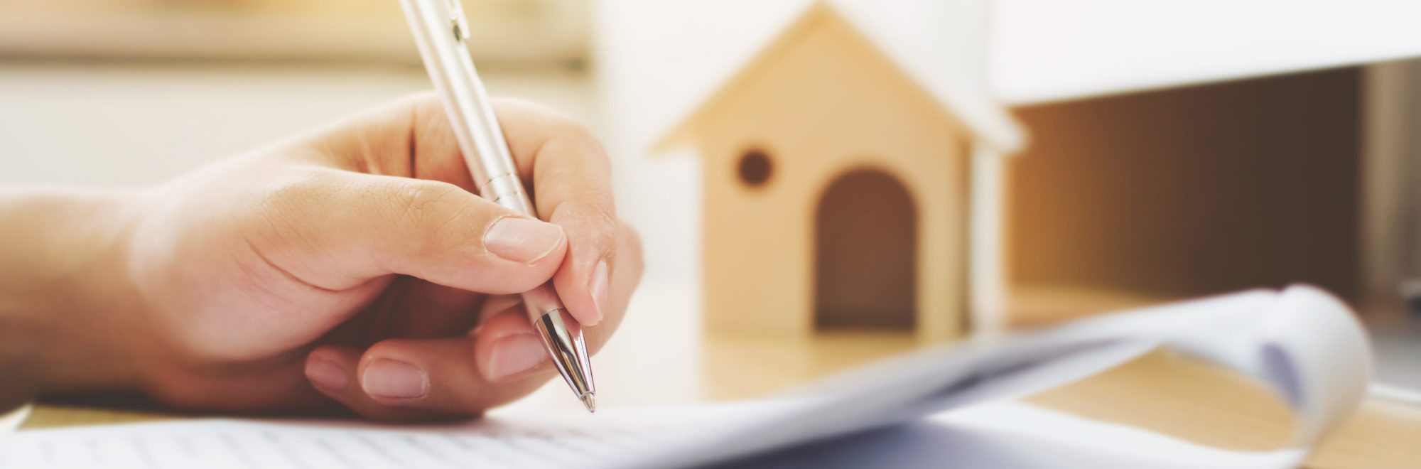 a hand holds a pen above a stack of papers. 