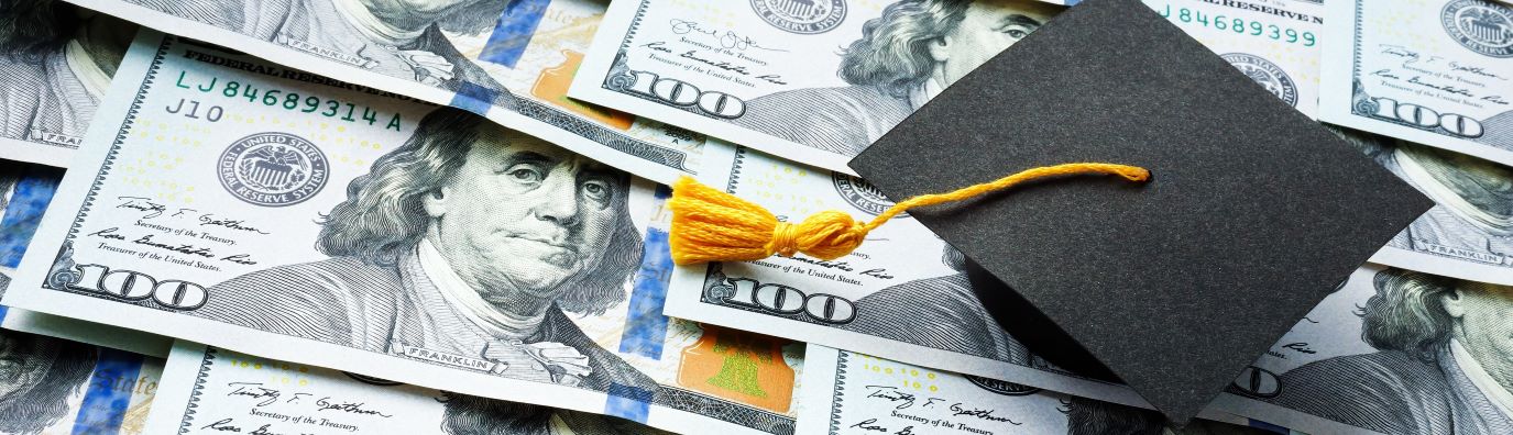 a graduation hats sitting on a spread of one-hundred dollar bills. 