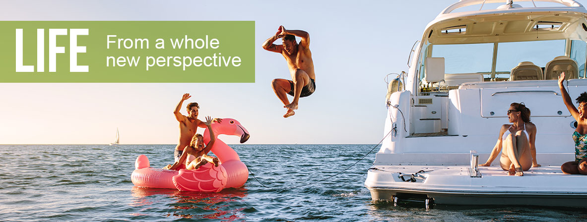 A group of friends enjoy a day at the lake. Two women are on a boat, one man is jumping from the boat into the water, a man a woman are in the water on an inflatable flamingo. The text on the image reads "Life from a whole new perspective"